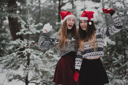 Two young teenage hipster girl friends together.Close up fashion portrait of two sisters hugs and having fun winter time,wearing sweater,best friends couple outdoors, snowy weatherの写真素材