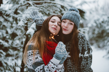 Two young teenage hipster girl friends together.Close up fashion portrait of two sisters hugs and having fun winter time,wearing sweater,best friends couple outdoors, snowy weatherの写真素材