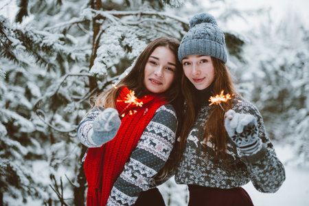 Two young teenage hipster girl friends together.Close up fashion portrait of two sisters hugs and having fun winter time,wearing sweater,best friends couple outdoors, snowy weatherの写真素材