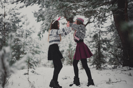 Two young teenage hipster girl friends together.Close up fashion portrait of two sisters hugs and having fun winter time,wearing sweater,best friends couple outdoors, snowy weatherの写真素材