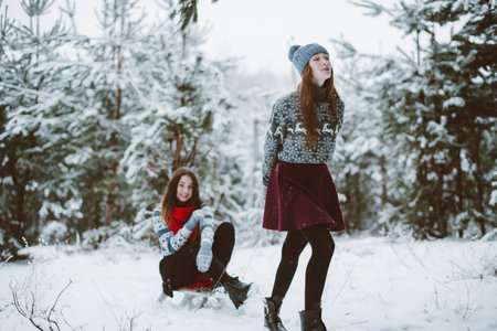Two young teenage hipster girl friends together.Close up fashion portrait of two sisters hugs and having fun winter time,wearing sweater,best friends couple outdoors, snowy weatherの写真素材