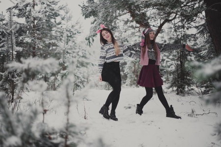Two young teenage hipster girl friends together.Close up fashion portrait of two sisters hugs and having fun winter time,wearing sweater,best friends couple outdoors, snowy weatherの写真素材
