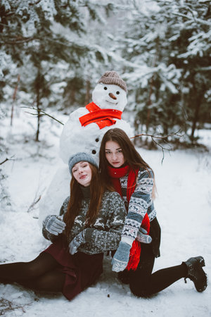 Two young teenage hipster girl friends together.Close up fashion portrait of two sisters hugs and having fun winter time,wearing sweater,best friends couple outdoors, snowy weatherの写真素材