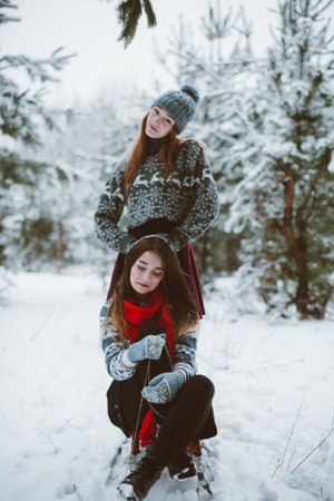 Two young teenage hipster girl friends together.Close up fashion portrait of two sisters hugs and having fun winter time,wearing sweater,best friends couple outdoors, snowy weatherの写真素材