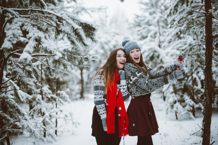 Two young teenage hipster girl friends together.Close up fashion portrait of two sisters hugs and having fun winter time,wearing sweater,best friends couple outdoors, snowy weatherの写真素材