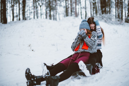 Two young teenage hipster girl friends together.Close up fashion portrait of two sisters hugs and having fun winter time,wearing sweater,best friends couple outdoors, snowy weatherの写真素材
