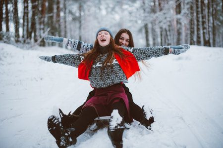 Two young teenage hipster girl friends together.Close up fashion portrait of two sisters hugs and having fun winter time,wearing sweater,best friends couple outdoors, snowy weatherの写真素材