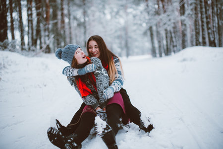 Two young teenage hipster girl friends together.Close up fashion portrait of two sisters hugs and having fun winter time,wearing sweater,best friends couple outdoors, snowy weatherの写真素材