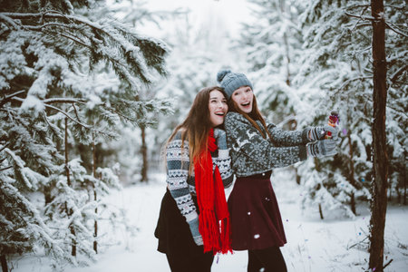 Two young teenage hipster girl friends together.Close up fashion portrait of two sisters hugs and having fun winter time,wearing sweater,best friends couple outdoors, snowy weatherの写真素材