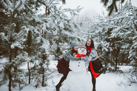 Two young teenage hipster girl friends together.Close up fashion portrait of two sisters hugs and having fun winter time,wearing sweater,best friends couple outdoors, snowy weatherの写真素材