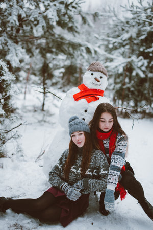 Two young teenage hipster girl friends together.Close up fashion portrait of two sisters hugs and having fun winter time,wearing sweater,best friends couple outdoors, snowy weatherの写真素材