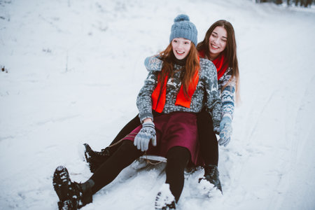 Two young teenage hipster girl friends together.Close up fashion portrait of two sisters hugs and having fun winter time,wearing sweater,best friends couple outdoors, snowy weatherの写真素材