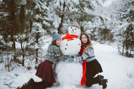 Two young teenage hipster girl friends together.Close up fashion portrait of two sisters hugs and having fun winter time,wearing sweater,best friends couple outdoors, snowy weatherの写真素材