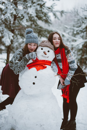 Two young teenage hipster girl friends together.Close up fashion portrait of two sisters hugs and having fun winter time,wearing sweater,best friends couple outdoors, snowy weatherの写真素材