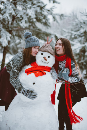 Two young teenage hipster girl friends together.Close up fashion portrait of two sisters hugs and having fun winter time,wearing sweater,best friends couple outdoors, snowy weatherの写真素材