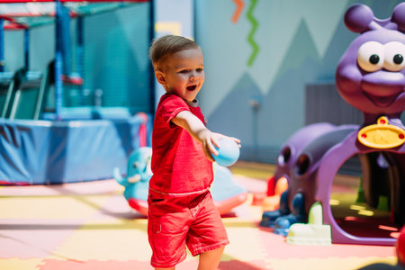 Happy laughing boy 1-2 years old having fun in ball pit on birthday party in kids amusement park and indoor play center. Child playing with colorful balls in playground ball pool. Activity toys for little kid.の写真素材