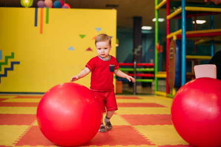 Happy laughing boy 1-2 years old having fun in ball pit on birthday party in kids amusement park and indoor play center. Child playing with colorful balls in playground ball pool. Activity toys for little kid.の写真素材