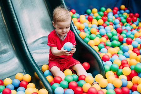 Happy laughing boy 1-2 years old having fun in ball pit on birthday party in kids amusement park and indoor play center. Child playing with colorful balls in playground ball pool. Activity toys for little kid.の写真素材