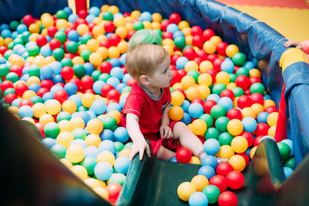 Happy laughing boy 1-2 years old having fun in ball pit on birthday party in kids amusement park and indoor play center. Child playing with colorful balls in playground ball pool. Activity toys for little kid.の写真素材