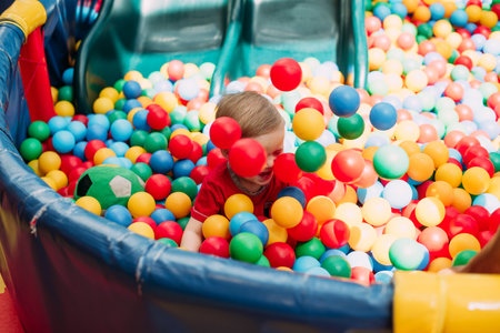 Happy laughing boy 1-2 years old having fun in ball pit on birthday party in kids amusement park and...