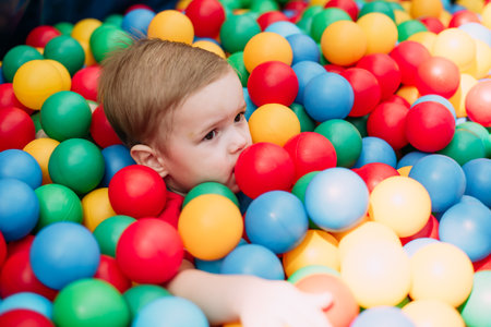 Happy laughing boy 1-2 years old having fun in ball pit on birthday party in kids amusement park and indoor play center. Child playing with colorful balls in playground ball pool. Activity toys for little kid.の写真素材