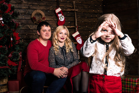 Beautiful young family in red having fun together for Christmas holidays, sitting on a living room...