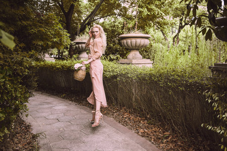 Sensual young blonde beautiful cute and elegant woman wearing pink sitting on the rock and looking into the camera over tropical green jungle palm background in China.の写真素材