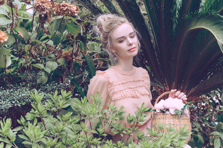 Sensual young blonde beautiful cute and elegant woman wearing pink sitting on the rock and looking into the camera over tropical green jungle palm background in China.の写真素材