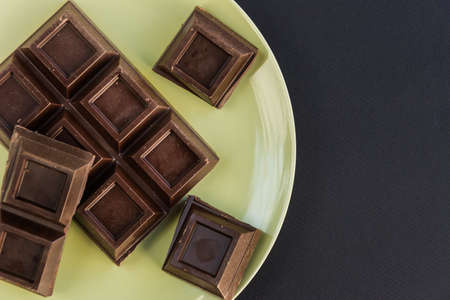 Broken dark chocolate bar slice in green plate