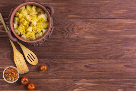 Top view of clay pots with hot roast potatoes and tomatoes on a wooden deskの写真素材