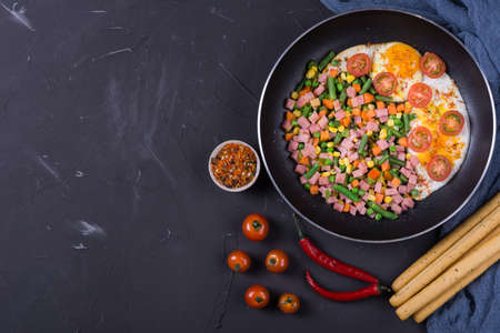 Fried eggs in iron pan with vegetables and hamの写真素材