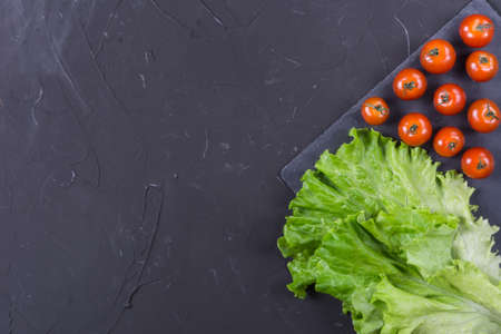 Red cherry tomatoes and lettuce leaves on dark backgroundの写真素材