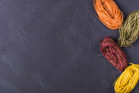 Raw colored tagliatelle and spaghetti on dark background