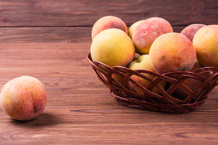 Ripe peaches fruit in wicker basket on wooden background