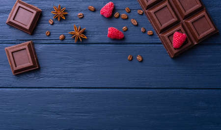 Broken chocolate bar slice with raspberry and coffee seeds on blue background