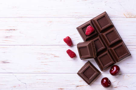 Broken chocolate bar slice with cherry and raspberry on white background