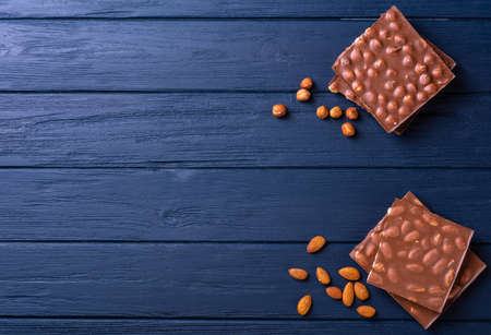 Broken chocolate bar slice with hazelnut and almond on blue background