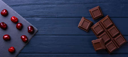 Broken chocolate bar slice with cherry on blue background