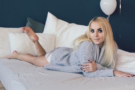 Beautiful and young woman in grey sweater on the bedの写真素材