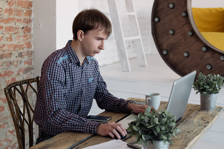 Young man working in office, sitting at desk, looking at laptop computer screenの写真素材