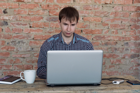 Young man working in office, sitting at desk, looking at laptop computer screenの写真素材