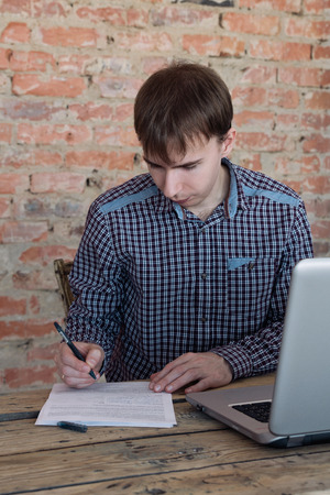 Young man working in office, sitting at desk, writing on paperの写真素材