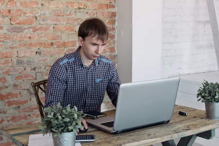 Young man working in office, sitting at desk, looking at laptop computer screenの写真素材