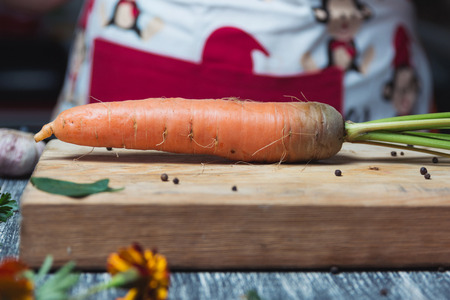 Carrots unwashed on a chopping board. Kitchen table, women in apron
