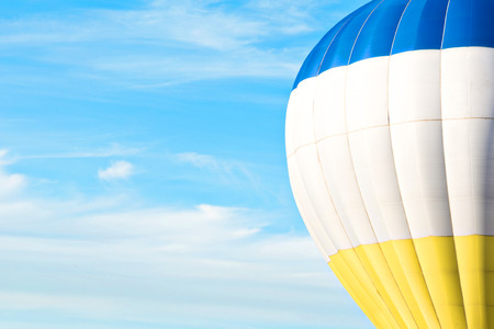 Multicolor (blue, white, yellow) air balloon in blue sky with cloudの写真素材