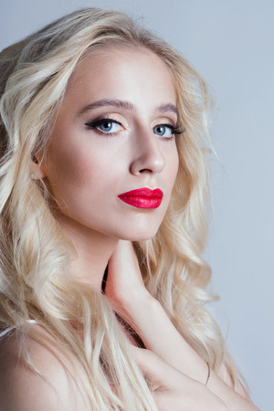 Fashion beautiful woman with blond curly hair. Beautiful portrait of sensual young woman model with glamour red lips make-up, eye arrow makeup, purity skinの写真素材