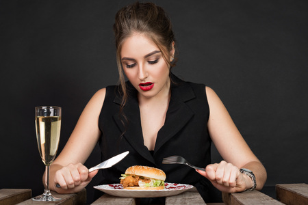 Fashionable young woman holding knife and fork and going to eat burgerの写真素材