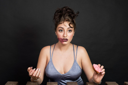 Fashionable confused young woman looking at tasty doughnuts. Face with the smeared lipstickの写真素材