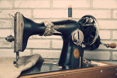 The handwheel vintage sewing machine. Black retro sewing machine on brick background. Wooden support