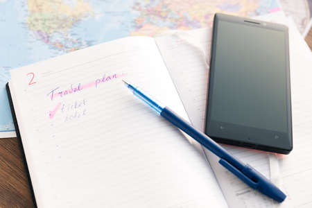 Open daily, pen and a phone  on the desktop with maps. Travel concept